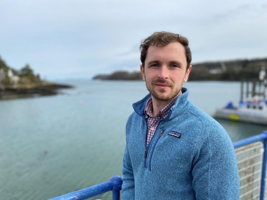 Young man stands on bridge with land and water out of focus behind him