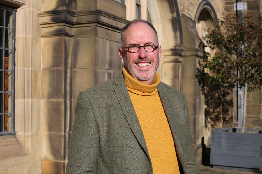 Professor Andrew Hiscock outside Main Arts' Terrace, wearing a yellow jumper