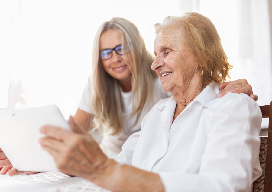 Younger member of family with an elderly member, looking at a tablet screen