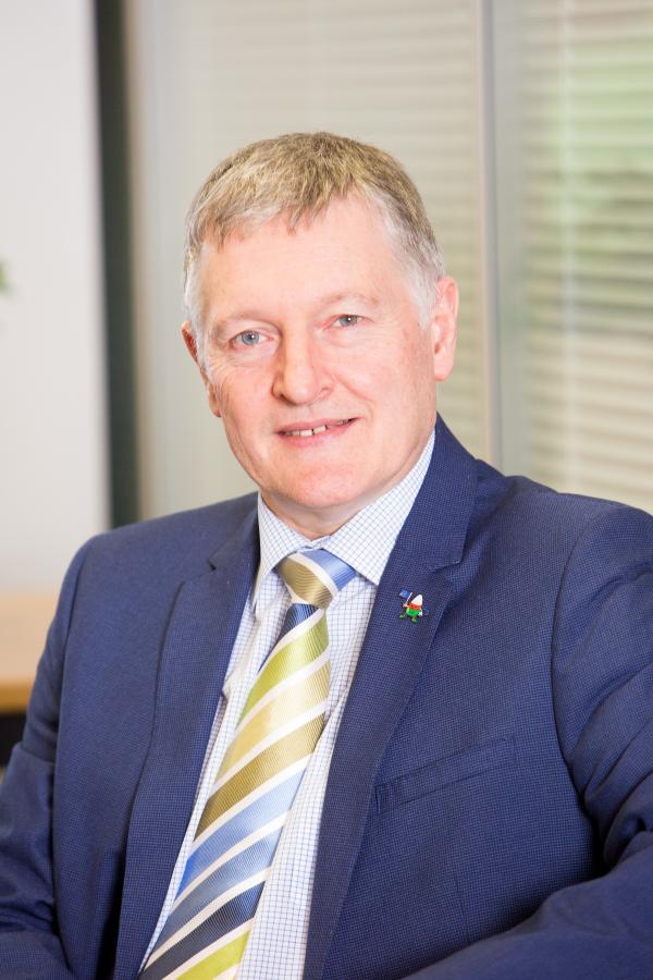 Close-up photo of Rheon Tomos in a navy suit and green and yellow tie