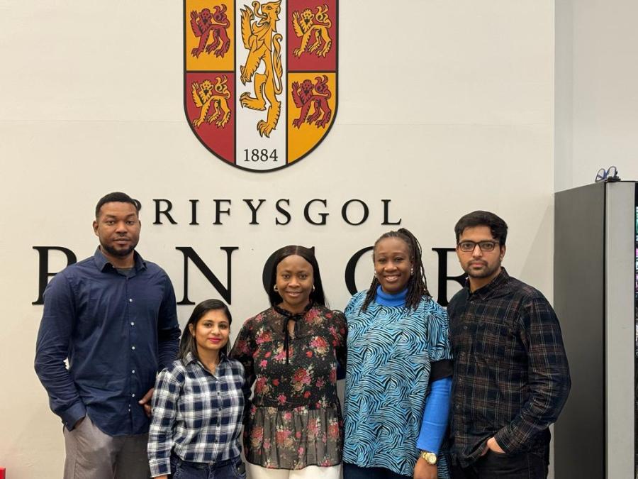 5 students standing in front of Bangor University crest