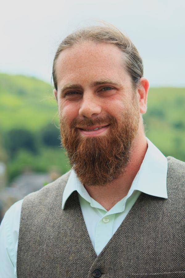 Llun ffurfiol o Dr Adam Coward yn gwenu, gyda barf a merlod