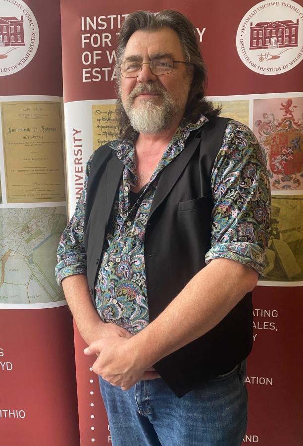Doctoral Researcher Peter stands in front of an ISWE banner.