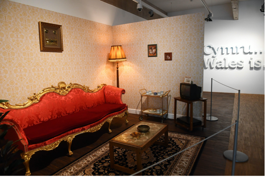 Photograph of installation by Nasia Sarwar-Skuse, a re-created sitting room with an elaborate red sofa in the middle. 