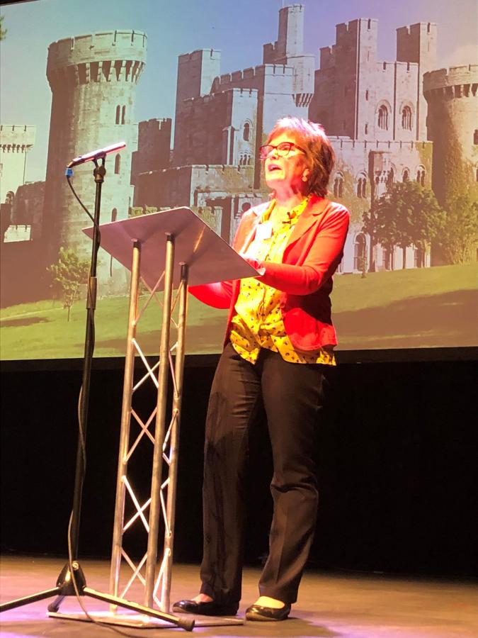 Marian Gwyn yn cyflwyno o flaen delwedd o Gastell Penrhyn.