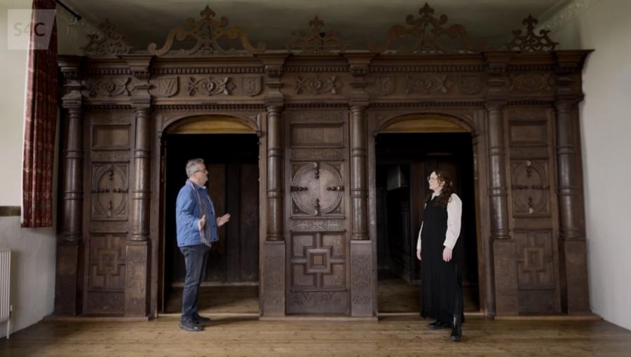 Mae'r cyflwynwyr Aled a Bethan yn sefyll o flaen y sgrin bren, Mannerist yn Neuadd Treowen.
