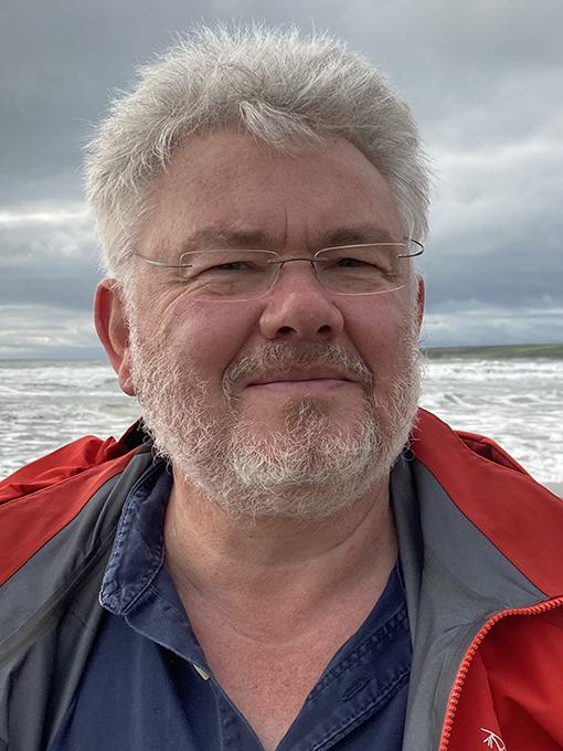Llun o'r Athro David Thomas gyda'r môr yn y cefndir