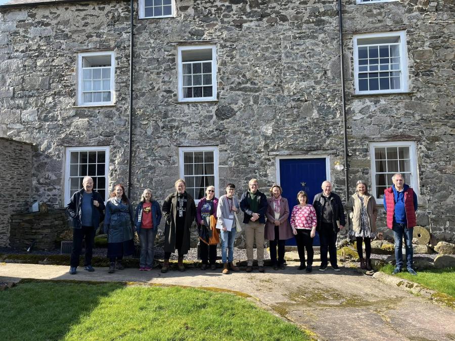 Group of twelve people stood in front of a stone house