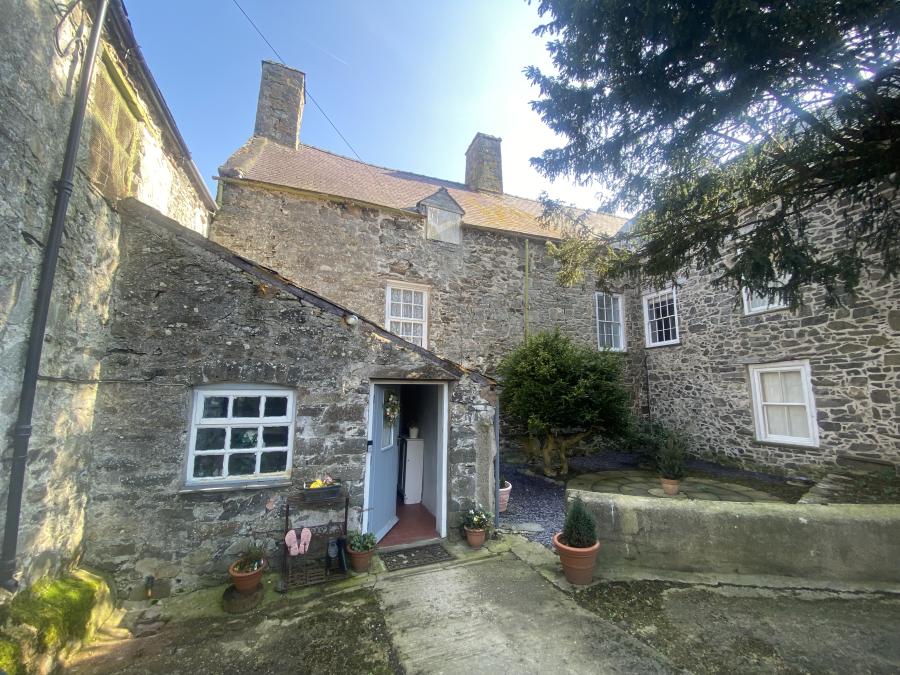 The back of a house with three ranges around a small court. There's a yew tree in the foreground and the blue porch door is ajar.