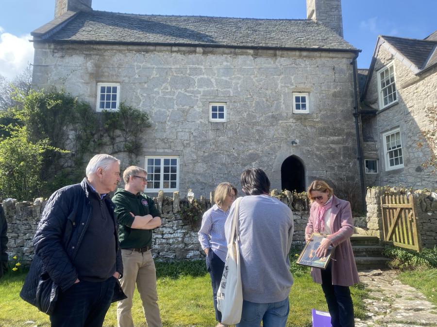 A group of five people talking, stood in front of a tall, stone house