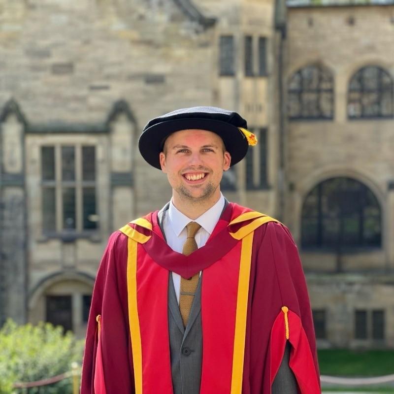 Photograph of Matthew in his red graduation gown.