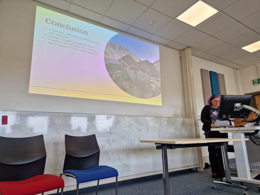 Anna stands behind a lectern and computer on the right, with her Powerpoint presentation to the left