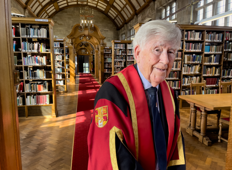 Llun o'r Athro David T Jones yn gwisgo gŵn graddio coch ac aur