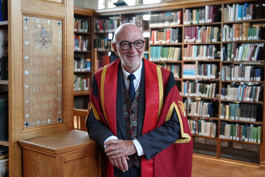 Llun o Gwyn Lewis Williams yn gwisgo gŵn graddio coch ac aur