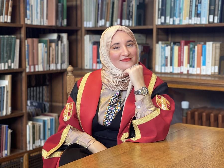 Llun o Hanan Issa yn gwisgo gŵn graddio coch ac aur