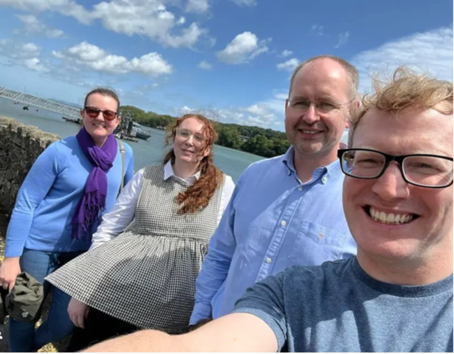 Four people taking a selfie in front of the Menai Straits, all smiling