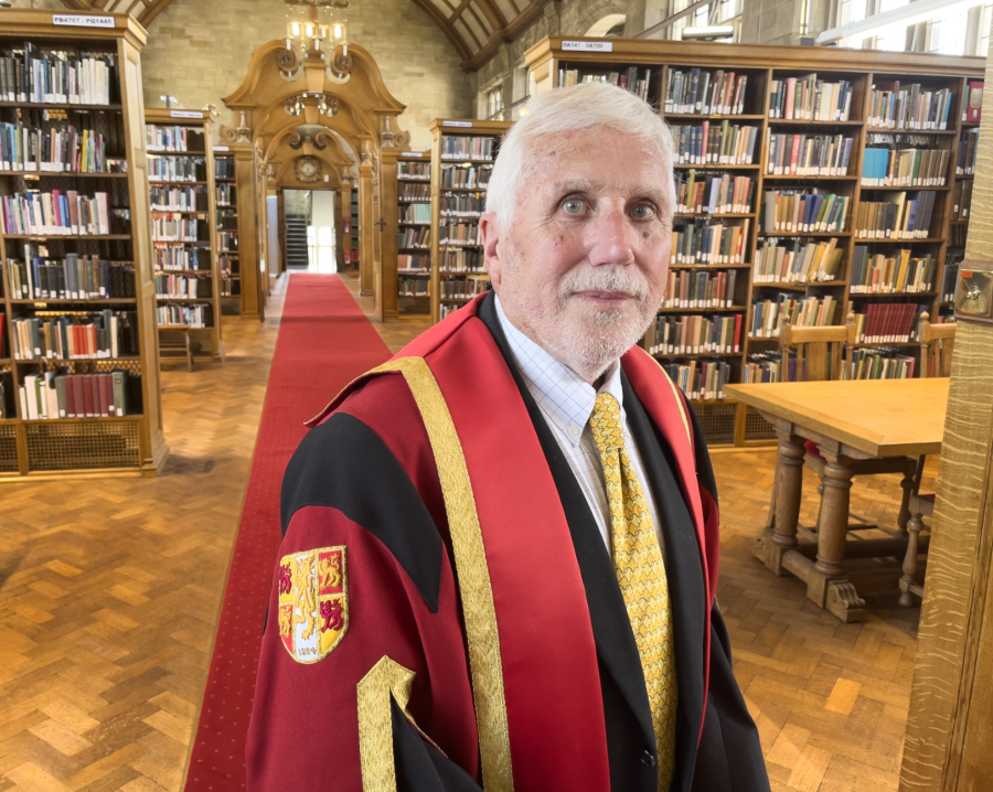 Llun o Dr Keith Hiscock yn gwisgo gŵn graddio coch ac aur