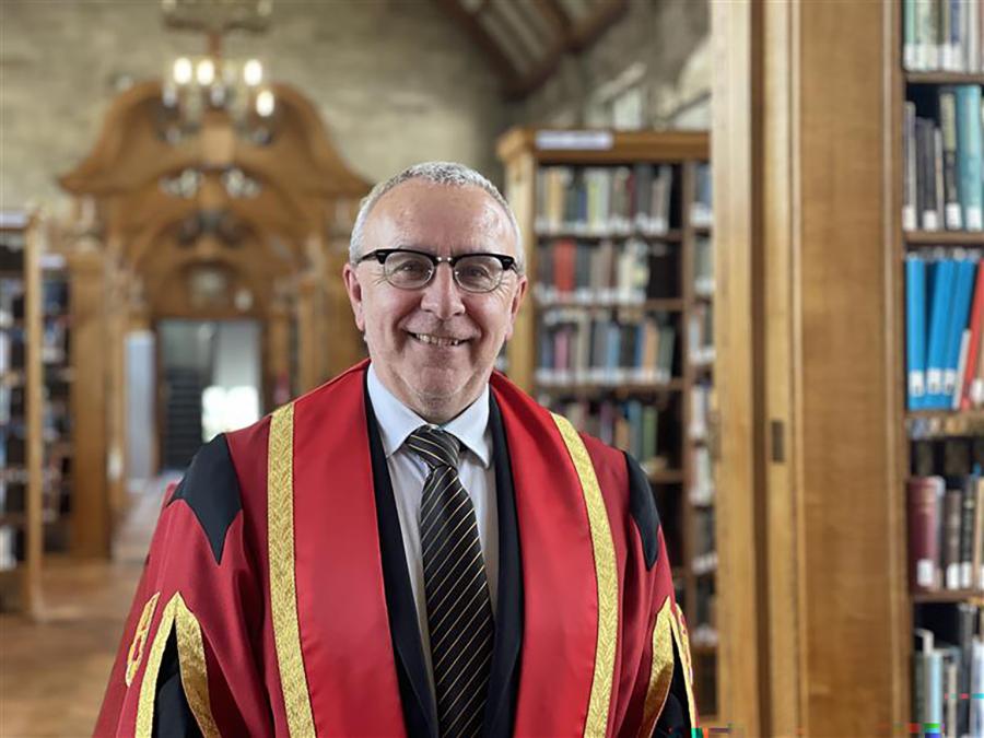 Llun o Pedr ap Llwyd yn gwisgo gŵn graddio coch ac aur