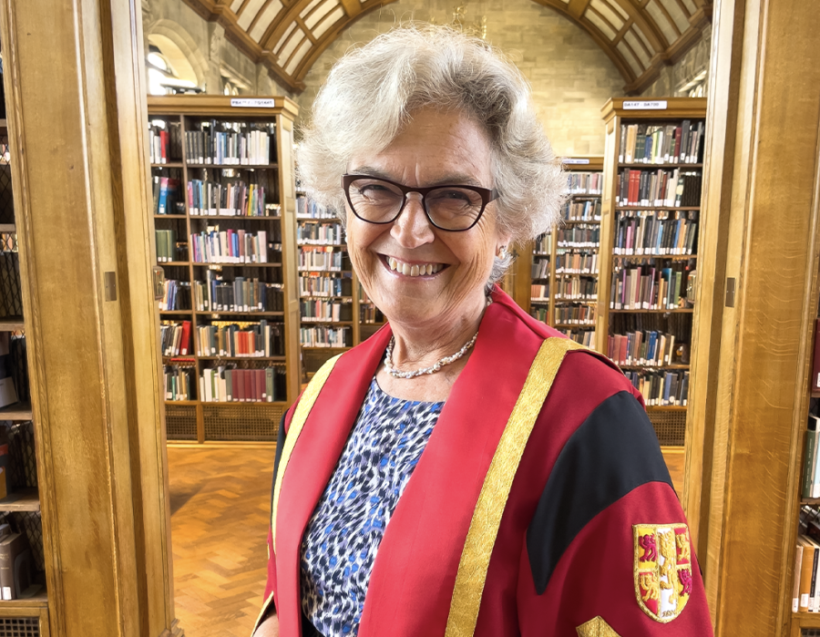 Llun o Alison Field mewn gŵn graddio coch ac aur