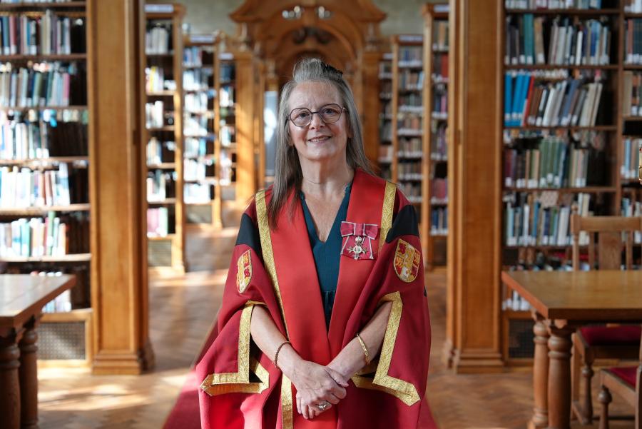 Llun o Sharon Manning MBE yn gwisgo gŵn graddio coch ac aur