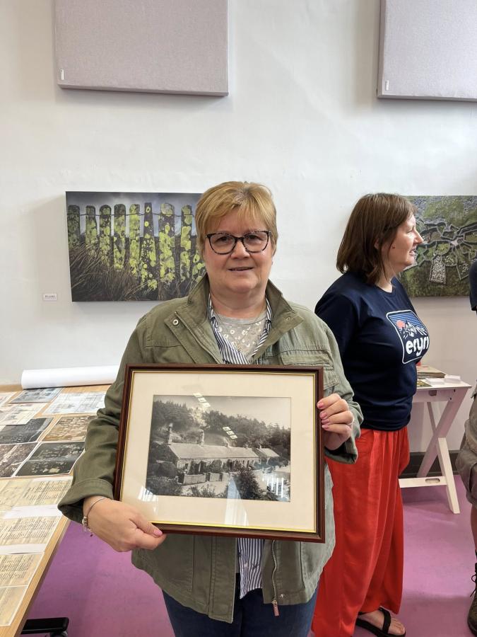 A woman holds a framed picture of a row of houses