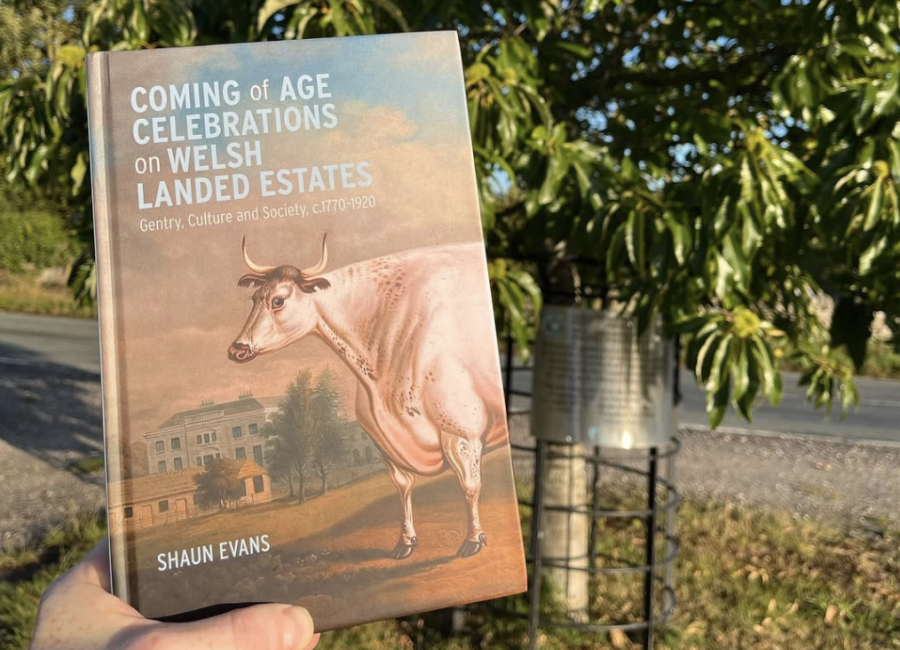 The new book, it's cover featuring a white ox, is held up in front of a tree