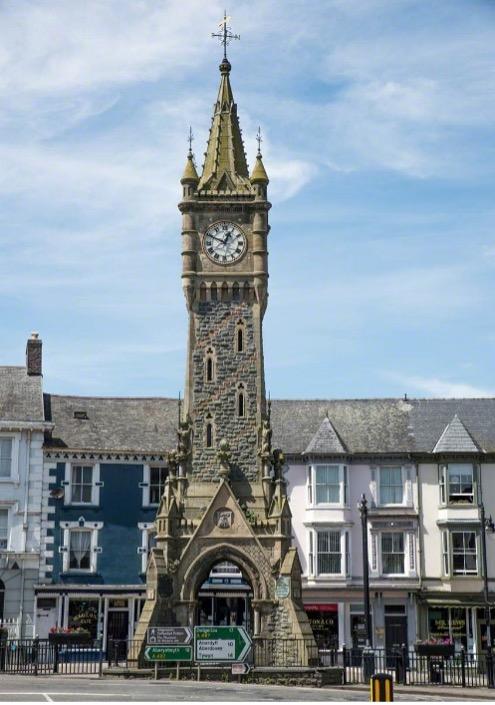 A stone clock tower with a row of terrace houses behind it.