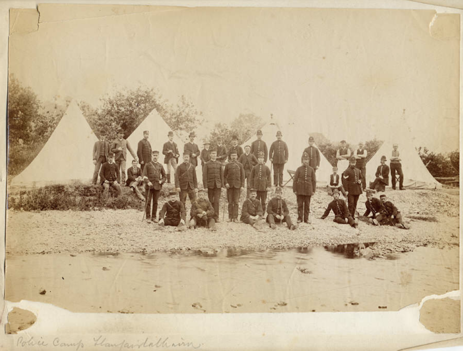 Llun sepia o grŵp mawr o heddweision yn sefyll o flaen pebyll gwyn