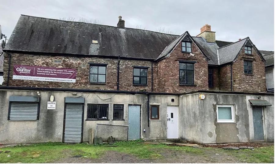 Cefn adeilad, lle mae'r llawr uchaf yn garreg a'r llawr isaf wedi'i rendro â choncrit.