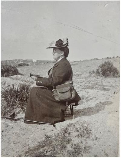 Sepia photograph of a woman sat amongst sand dunes