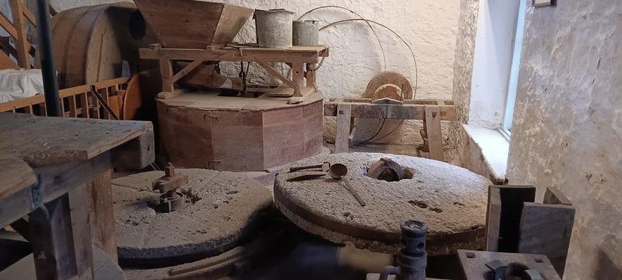 Ffotograff o tu mewn i felin hanesyddol gyda dau faen melin mawr, crwn.