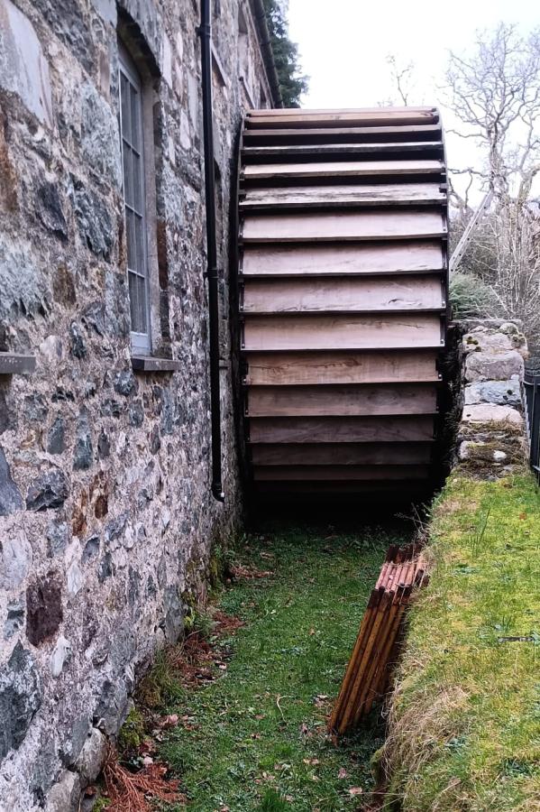 Ffotograff o olwyn ddŵr bren ar ochr adeilad carreg.