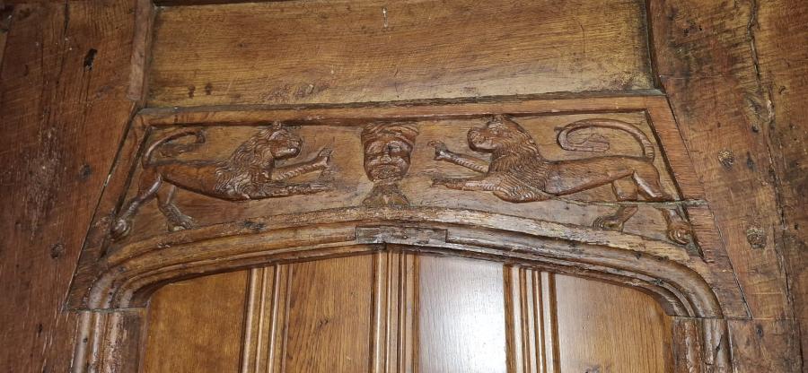 Ffotograff o gerfiad pren uwchben drws.