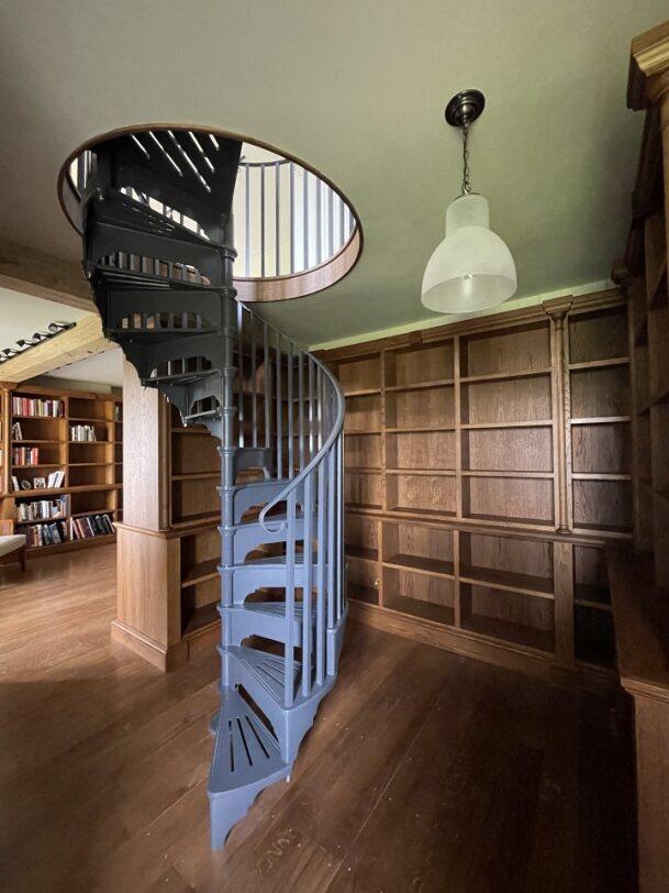 Photograph of a room lined with wooden shelves. There is an iron spiral staircase in the middle of the room.
