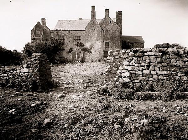 Black and white photograph of a derelict house, with part of the roof missing. 