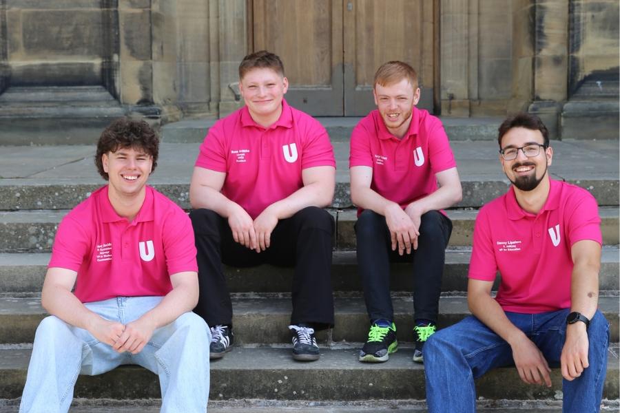 Student Officers for 2026-27 wearing fuchsia t-shirts and sitting on some steps outside the Main Arts Building. 